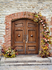 An old double door in a stone wall, decorated with flowers.