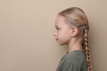 Profile portrait of cute little girl on beige background. Space for text