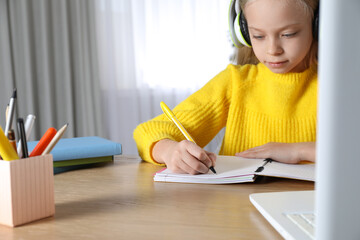 Cute little girl with laptop studying online at home, space for text. E-learning
