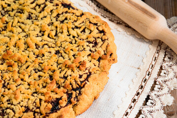 Appetizing grated pie with jam on a napkin. Close-up of a baked pie with a golden crust.Wooden table, light from the window.
