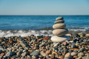 Beautiful pyramid of pebbles on the seashore with splashing waves on a sunny day, copy the space. Concept of balance, harmony