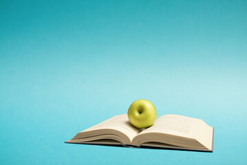 Education knowledge concept still life image with free space for text. Green apple on an open book on blue background.