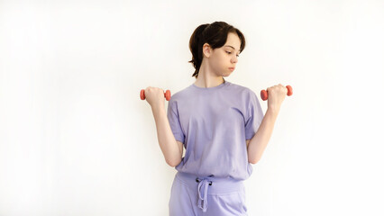 A teenager in sportswear with dumbbells in his hands. A young beautiful girl does exercises at home. Playing sports. Healthy body image concepts