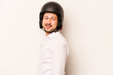 Hispanic business man going to work with motorcycle isolated on white background looks aside smiling, cheerful and pleasant.