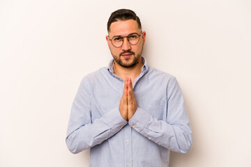 Young hispanic man isolated on white background praying, showing devotion, religious person looking for divine inspiration.