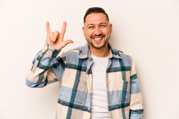 Young hispanic man isolated on white background showing a horns gesture as a revolution concept.