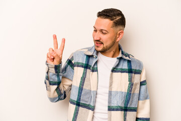 Young hispanic man isolated on white background joyful and carefree showing a peace symbol with fingers.