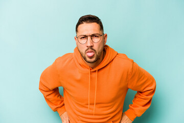 Young hispanic man isolated on blue background funny and friendly sticking out tongue.