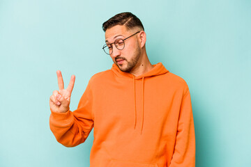 Young hispanic man isolated on blue background joyful and carefree showing a peace symbol with fingers.