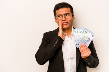 Young hispanic business man holding banknotes isolated on white background is saying a secret hot braking news and looking aside