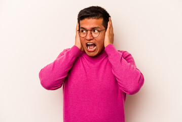 Young hispanic man isolated on white background covering ears with hands trying not to hear too loud sound.