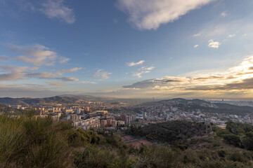 Picturesque landscape of Barcelona from the hill in the early morning. Sunbeams through the clouds. Dramatic sky over the city. Autumn in Barcelona, Spain.