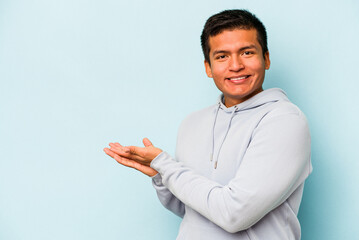 Young hispanic man isolated on blue background looking sideways with doubtful and skeptical expression.