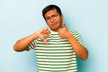 Young hispanic man isolated on blue background showing thumbs up and thumbs down, difficult choose...