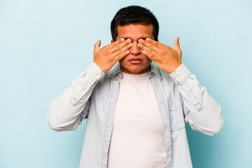 Young hispanic man isolated on blue background afraid covering eyes with hands.