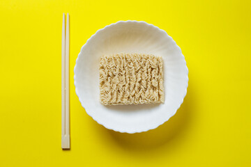 raw instant noodles in white plate and chopsticks. on a yellow background.