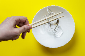 a female hand holds headphones with chopsticks over a plate. headphone wires symbolize noodles. joke photo.
