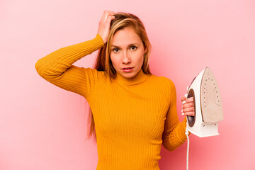 Young caucasian woman holding iron isolated on pink background being shocked, she has remembered...
