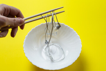 a female hand holds headphones with chopsticks over a plate. headphone wires symbolize noodles....