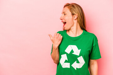 Young volunteer woman isolated on pink background points with thumb finger away, laughing and...