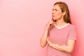 Young caucasian woman isolated on pink background looking sideways with doubtful and skeptical expression.