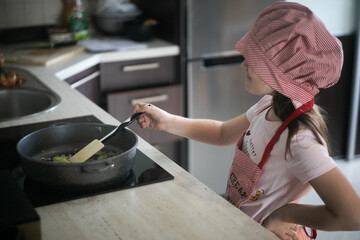 Fototapeta Dziewczynka stoi przed kuchenką i gotuje na patelni  obraz