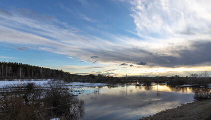 Epic spring landscape by the river. The flood of the river in early spring. A colorful sunset is reflected in the water. March evening landscape.