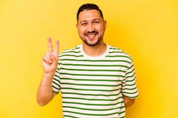 Young hispanic man isolated on yellow background showing victory sign and smiling broadly.