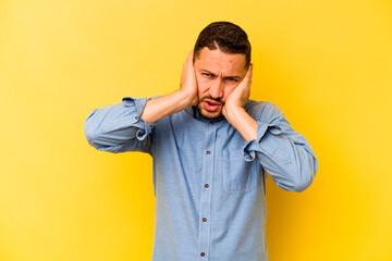 Young hispanic man isolated on yellow background covering ears with hands.