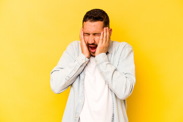 Fototapeta premium Young hispanic man isolated on yellow background covering ears with hands trying not to hear too loud sound.