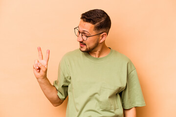 Fototapeta premium Young hispanic man isolated on beige background joyful and carefree showing a peace symbol with fingers.