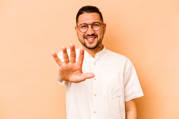 Young hispanic man isolated on beige background smiling cheerful showing number five with fingers.