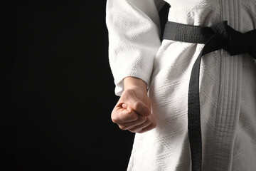 Man wearing keikogi and black belt on dark background, closeup view with space for text. Martial...