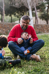 Father enjoying playing with his children sitting on the grass outdoors.