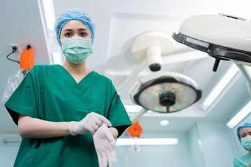 Portrait of Asian surgeon with medical mask standing and wearing medical gloves in operation...