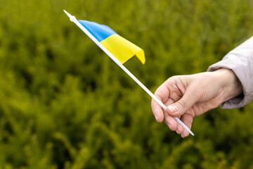 Closeup of woman hand showing flag on nature background. Woman with yellow and blue flag of Ukraine. Independence Day, Constitution day. Invasion in Ukraine. Russian attack, Patriotism symbol.