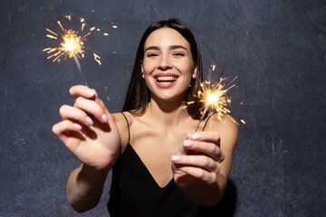 Portrait of a smiling brunette in a black dress with sparklers