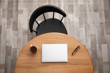 Round wooden table with cup of tea, computer tablet, and eyeglasses near black chair indoors, top...