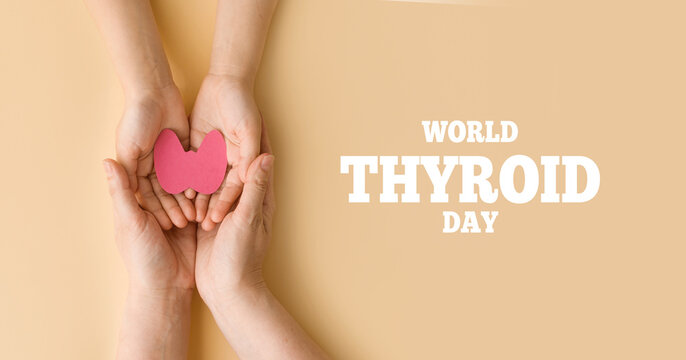 World Thyroid Day. Mom's and baby's hands hold paper form of the thyroid gland on beige background. Problems with thyroid. Polycystic disease. World cancer day