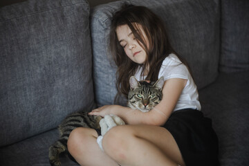 Młoda dziewczynka odpoczywająca z kotem na sofie - obrazy, fototapety, plakaty