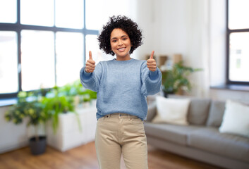people, real estate and mortgage concept - happy smiling woman in blue sweater and jeans showing thumbs up gesture over home living room background - Powered by Adobe