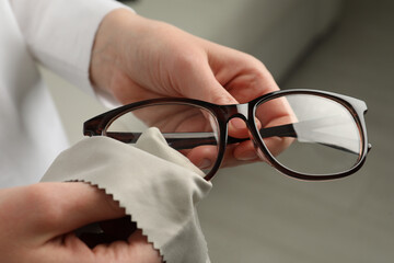 Woman cleaning glasses with microfiber cloth at home, closeup