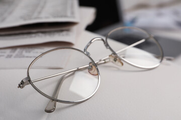 Glasses and newspapers on armrest indoors, closeup