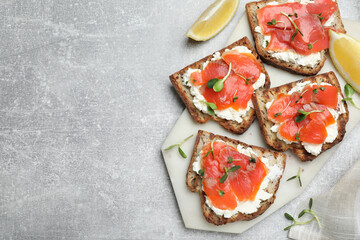 Delicious sandwiches with cream cheese, salmon and microgreens on light grey table, flat lay. Space for text