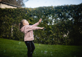 Fototapeta Dziewczynka bawi się bańkami na podwórku obraz