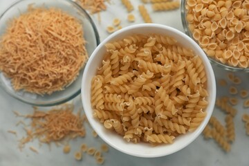 Different types of pasta on white marble table, flat lay