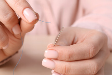 Woman threading sewing needle at table, closeup