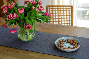 bowl with walnuts and vase with tulips on wooden table indoors