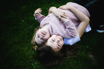 Dwie siostry przytulają się i leżą plecami na zielonej trawie - obrazy, fototapety, plakaty