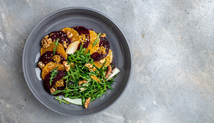 Arugula, Beet and oranges salad with walnuts on plate with fork, dressing and spices on gray background, Vitamin salad. Proper nutrition. place for text, top view